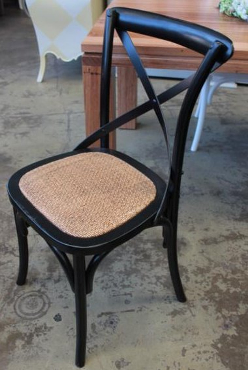 Featuring a durable rattan seat, the Cross Back Chair from Canalside Interiors in distressed black adds a touch of elegance to a living room with its coastal and classical design
