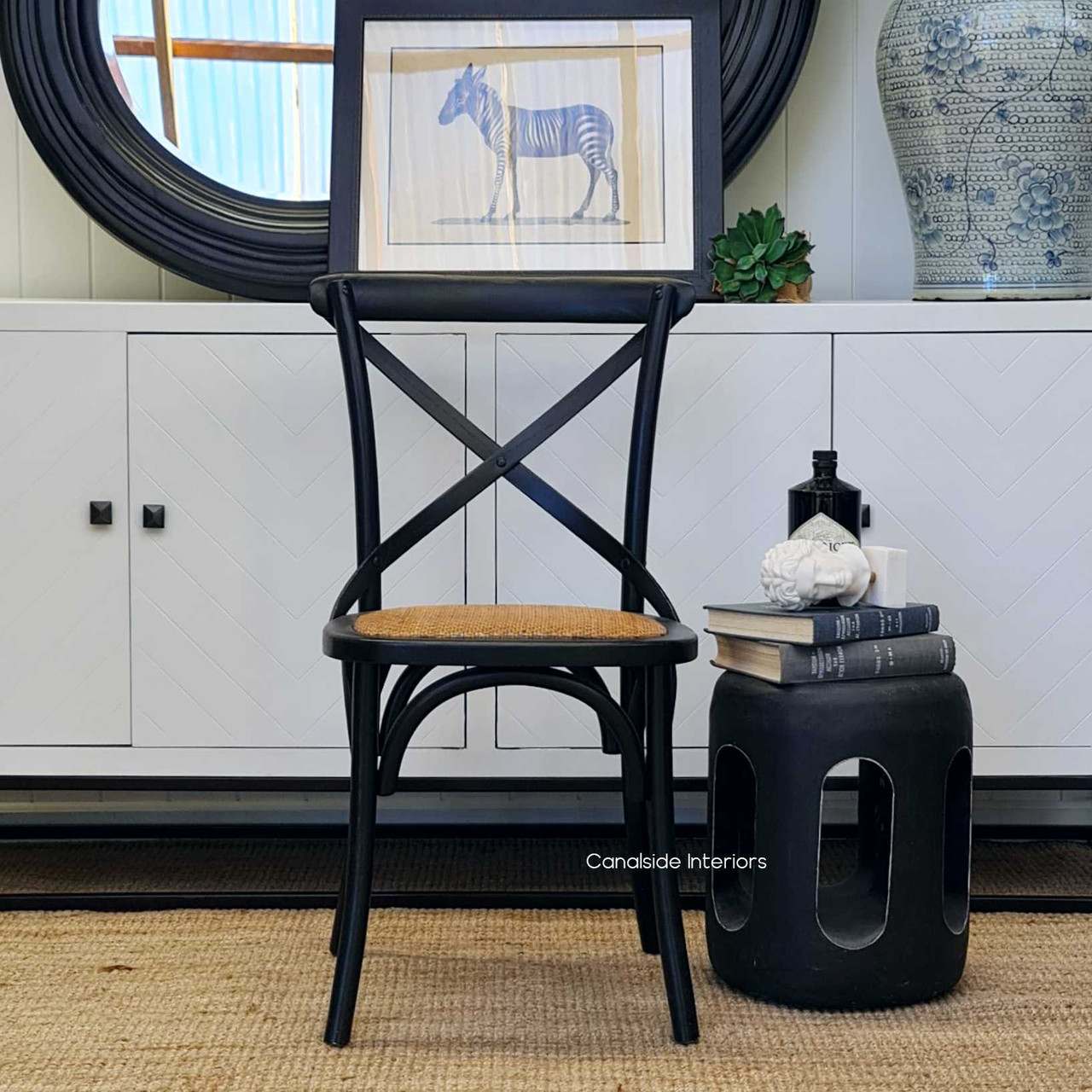 This side angle reveals the elegant lines and sturdy construction of the Distressed Black Cross Back Chair from Canalside Interiors, ideal for adding timeless quality to your lounge room