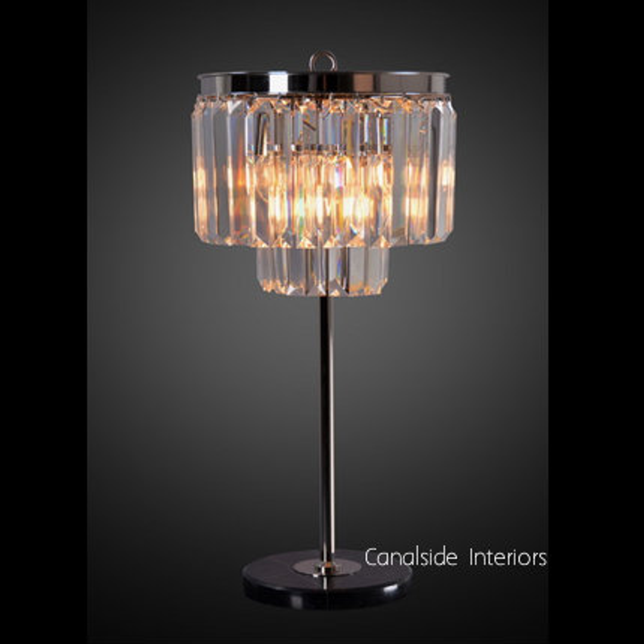 The Odeon Table Lamp from Canalside Interiors, with its distressed grey finish and sparkling prisms, adds Art Deco elegance to any bedroom