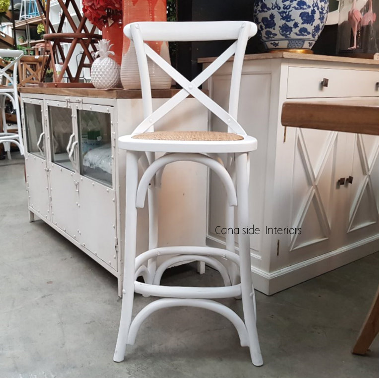Elegantly poised, this Cross Back Kitchen Stool in Distressed White enriches the serene bedroom setting with its coastal elegance