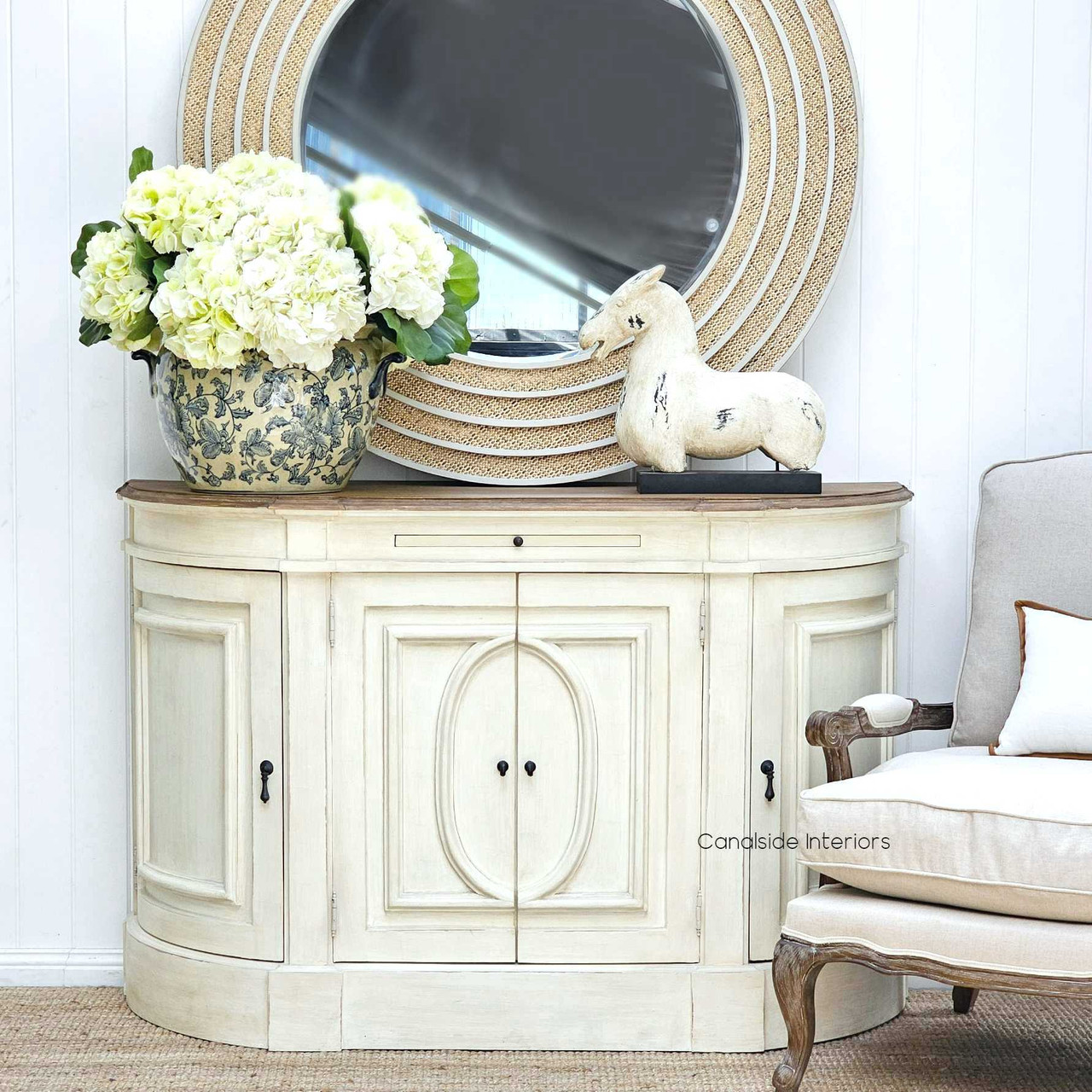 Elegantly staged at Canalside Interiors, the Bastian Sideboard is paired with a round mirror, emphasizing its plantation style and functional elegance