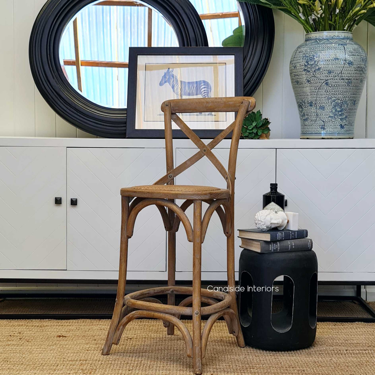 The oatmeal Cross Back Stool is poised elegantly in a kitchen setting, its silhouette a testament to the timeless design and quality construction