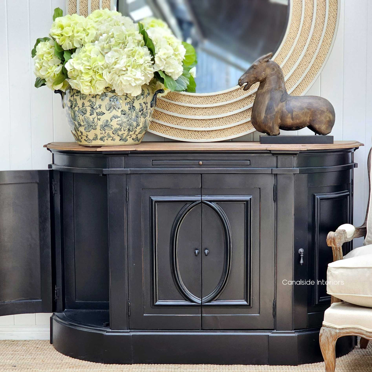 Distressed charcoal black sideboard as a focal point in a lounge room, accessorized with bright floral arrangements and Hamptons-inspired decor - Canalside Interiors