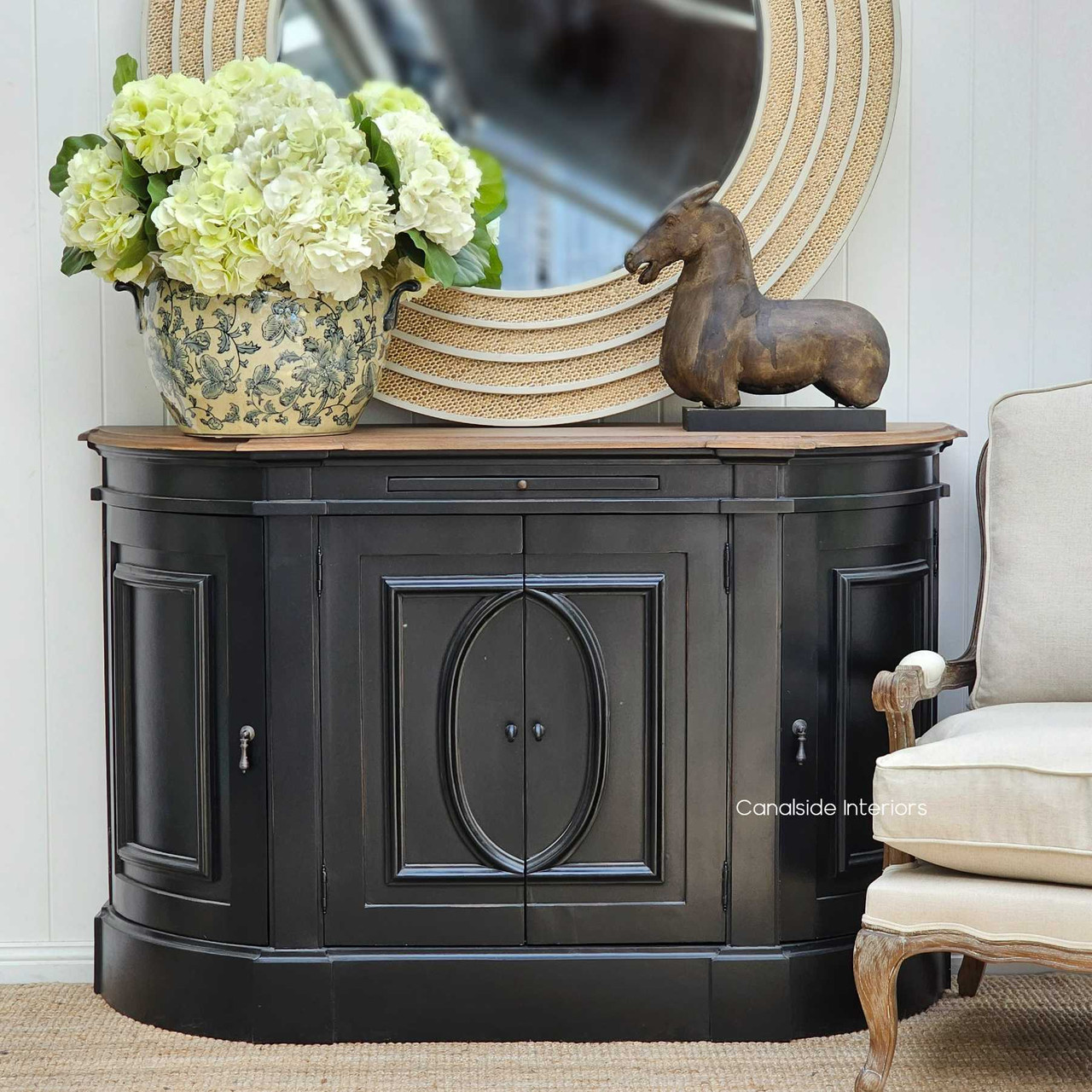 The Bastian Small Sideboard in charcoal black, standing elegantly in a serene bedroom, its weathered oak top a testament to Canalside Interiors' commitment to timeless quality.