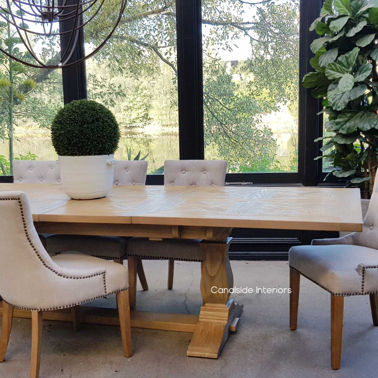 Front view of the Balmoral Parquetry Extension Dining Table set in a sunlit dining room, showcasing the natural parquetry top and the contrasting distressed grey base.
