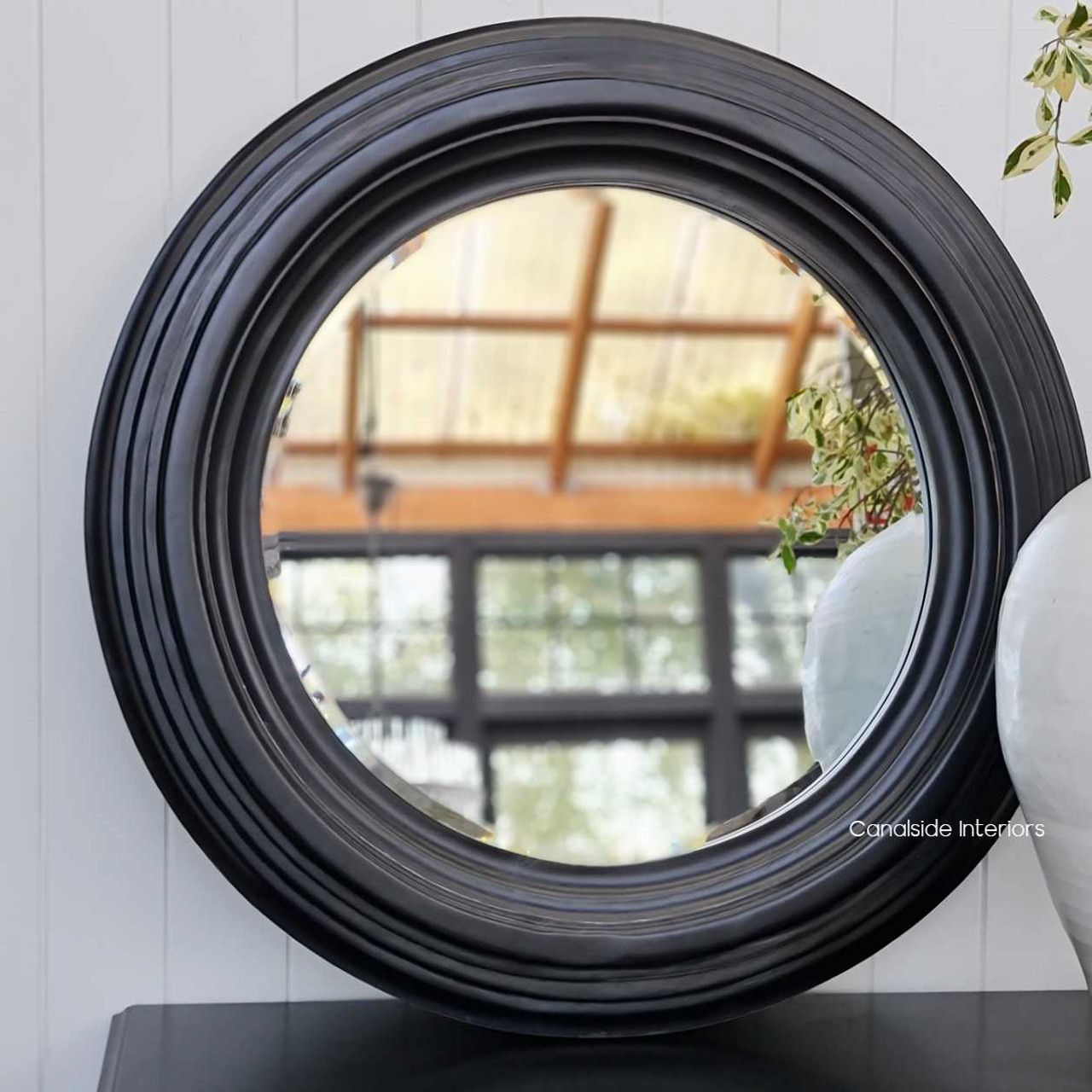View of the Aspen Mirror at Canalside Interiors, showcasing its classic round design and distressed black finish.