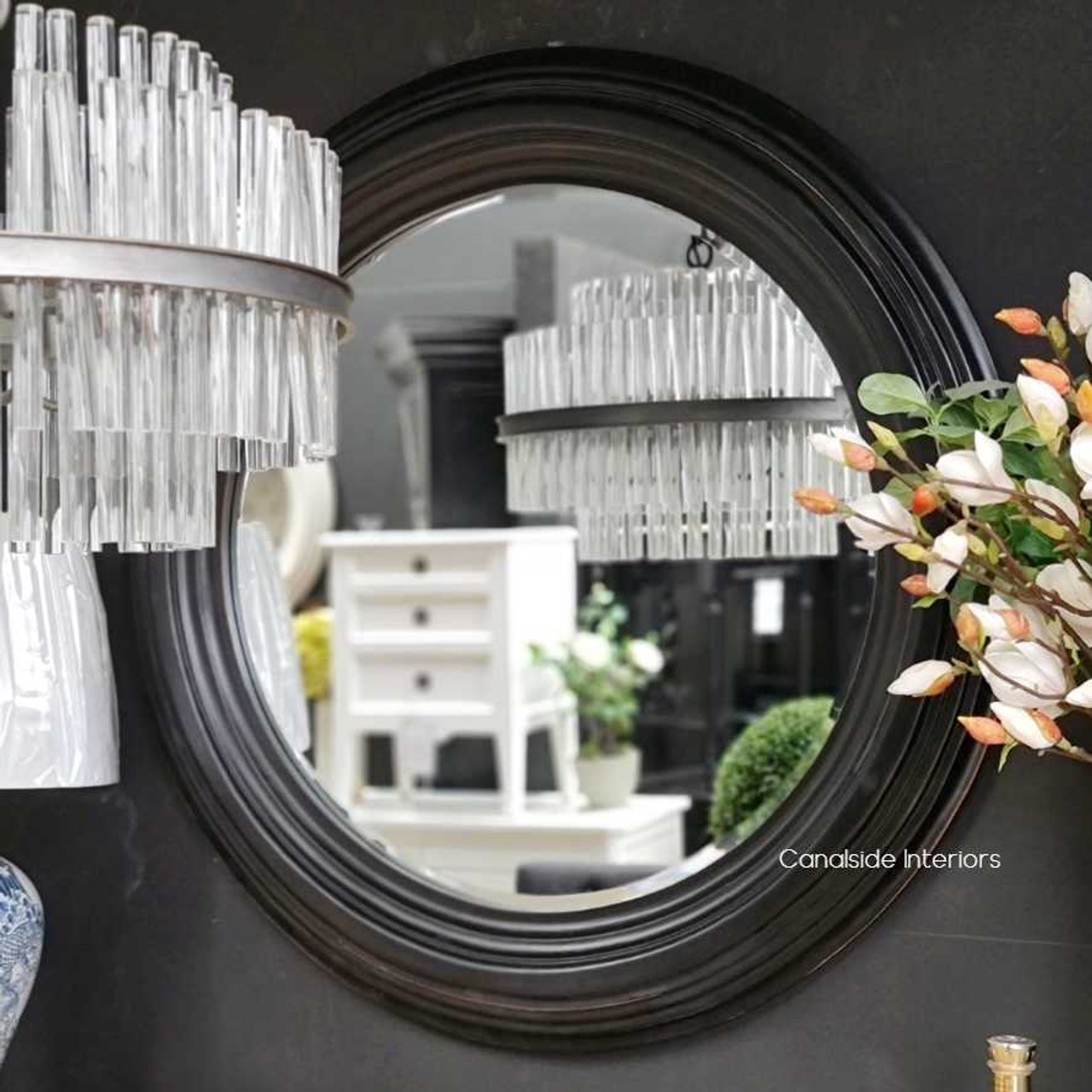 View of the Aspen Mirror at Canalside Interiors, showcasing its classic round design and distressed black finish.