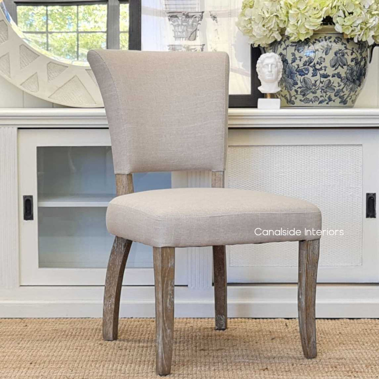 Side profile of the Mimi Dining Chair, showcasing the beautiful curve of its weathered oak legs and the depth of its cream upholstery.