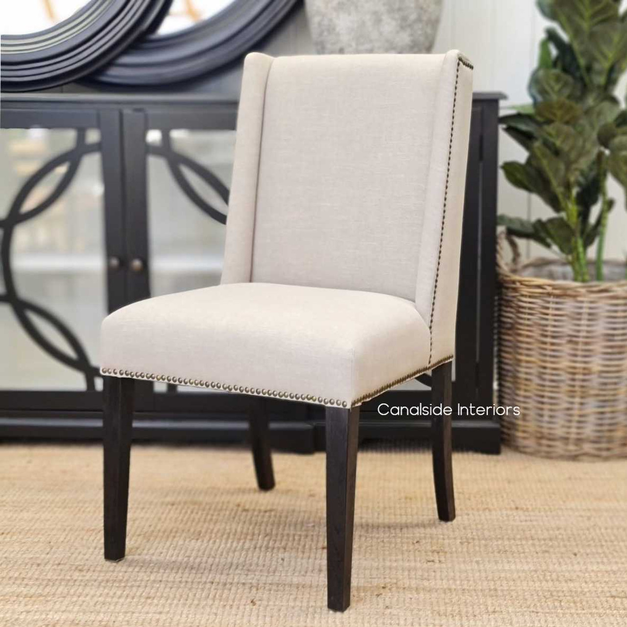 Leclerc Dining Chair's silhouette against a dramatic backdrop, highlighting the contrast between the cream upholstery and the chair's dark leg finish.