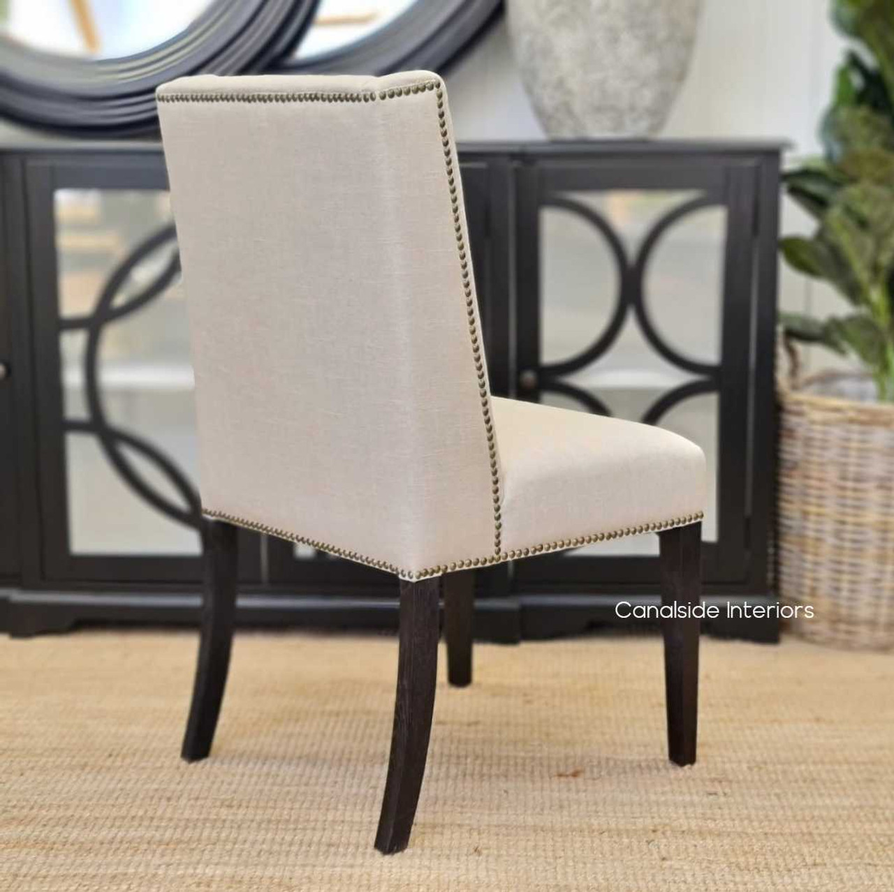 The Leclerc Dining Chair captured from behind, showcasing the winged back silhouette and brass stud embellishments, set against a minimalist dining room interior.