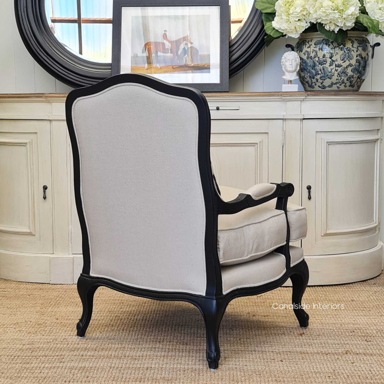 Rear view of the armchair, showing off the contrast between the cream upholstery and distressed black frame.