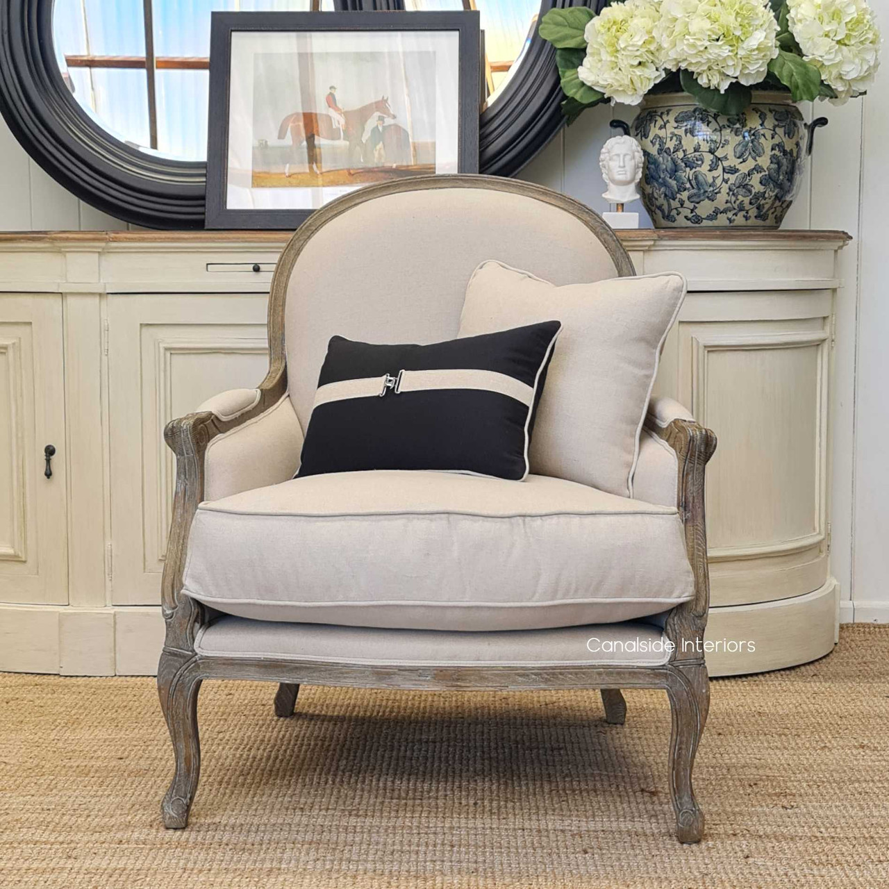 Front view of the Monette Occasional Armchair in weathered oak with charcoal/black upholstery, showcasing its intricate hand-carved details and plush seating, perfect for a Hamptons-style living room.