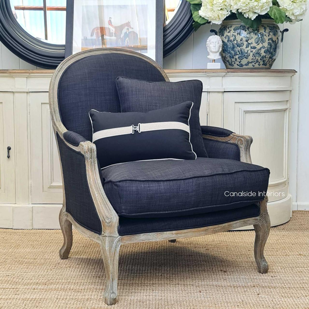View of the Monette Occasional Armchair in charcoal/black, highlighting the intricate hand-carved weathered oak frame and plush upholstery, ideal for a Hamptons-style living room.