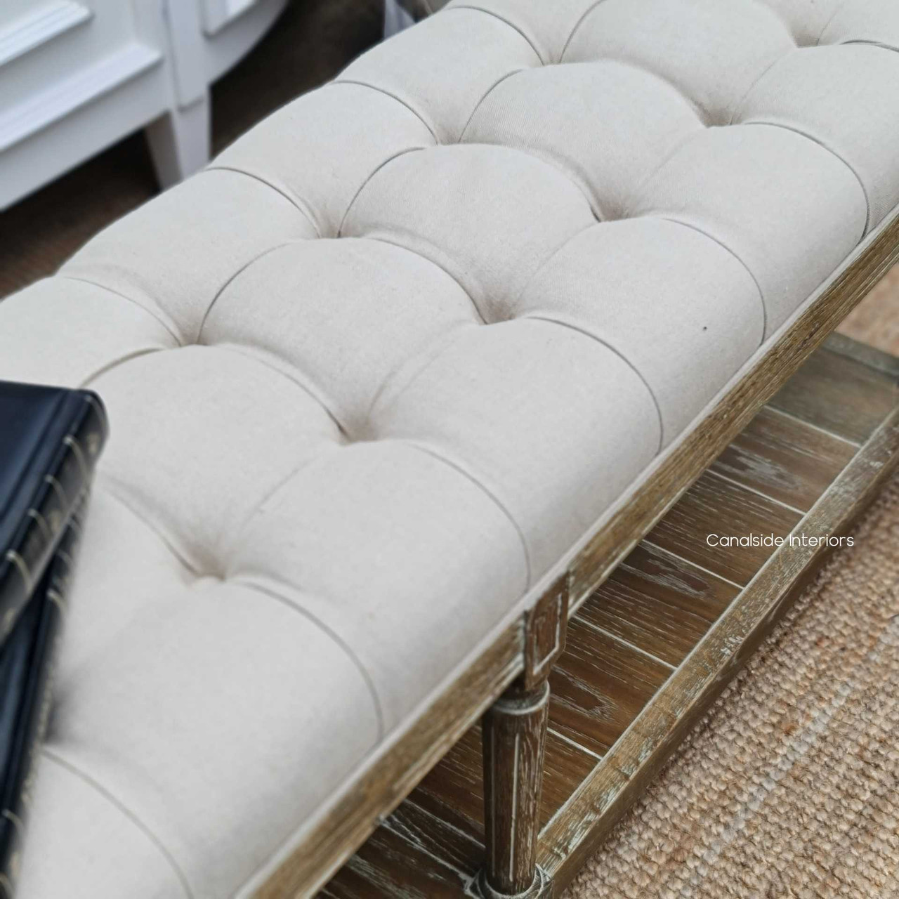 Close-up of the weathered oak base and cream fabric, highlighting the luxurious button tufting detailing that adds texture and depth.