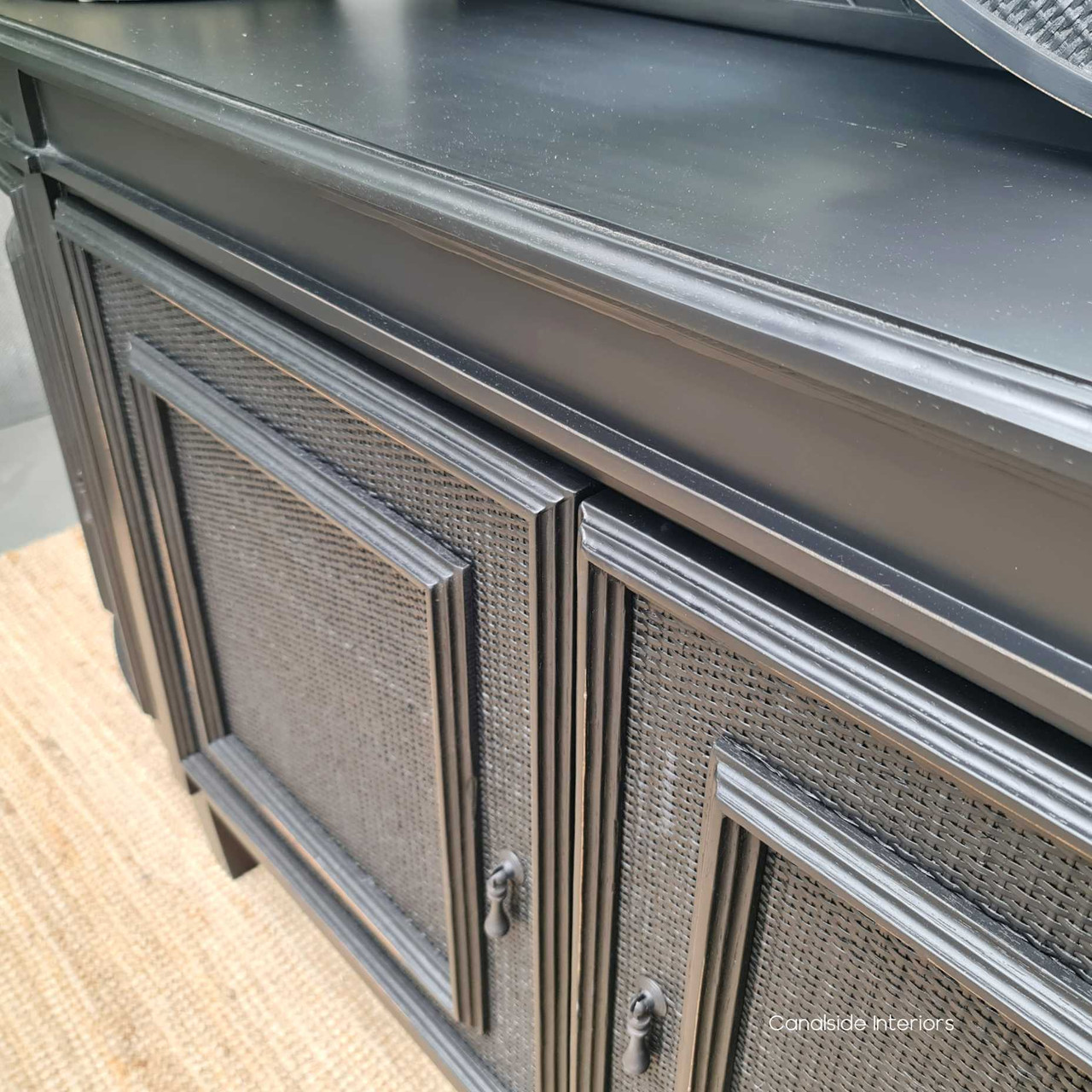 The Francia Rattan Sideboard in distressed black/charcoal seamlessly blends with a coastal-themed lounge room, embodying the sophistication of Canalside Interiors