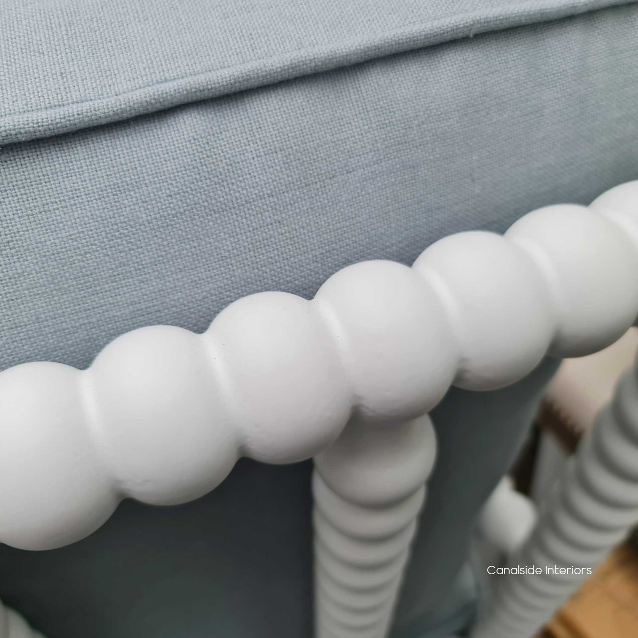 Detail shot of the corbeled bobbin arm and pastel blue linen blend upholstery, showcasing the soft texture and inviting color that adds charm to any room.
