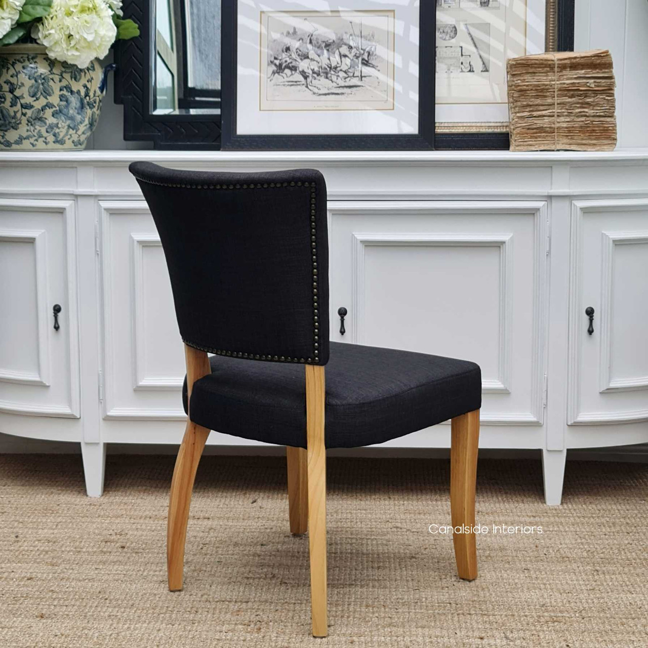 Rear view of the Mimi Dining Chair, focusing on the harmonious integration of design elements like brass studs and distressed natural legs.