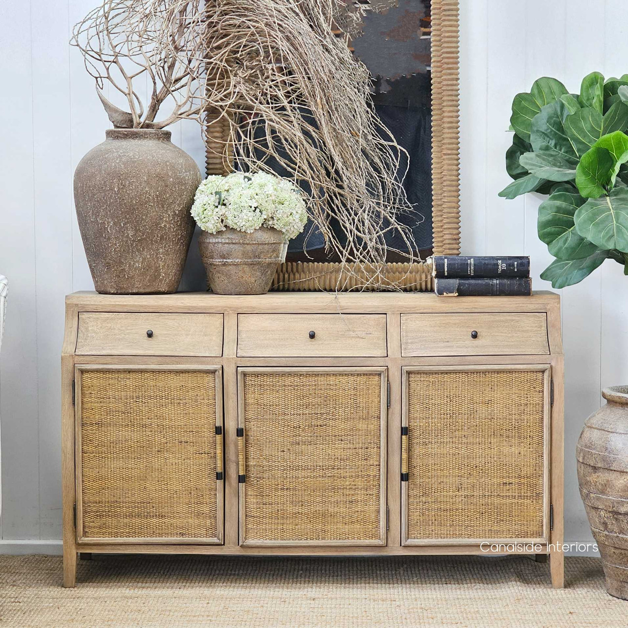 View of the sideboard styled in a hallway, paired with earthy ceramics and greenery.