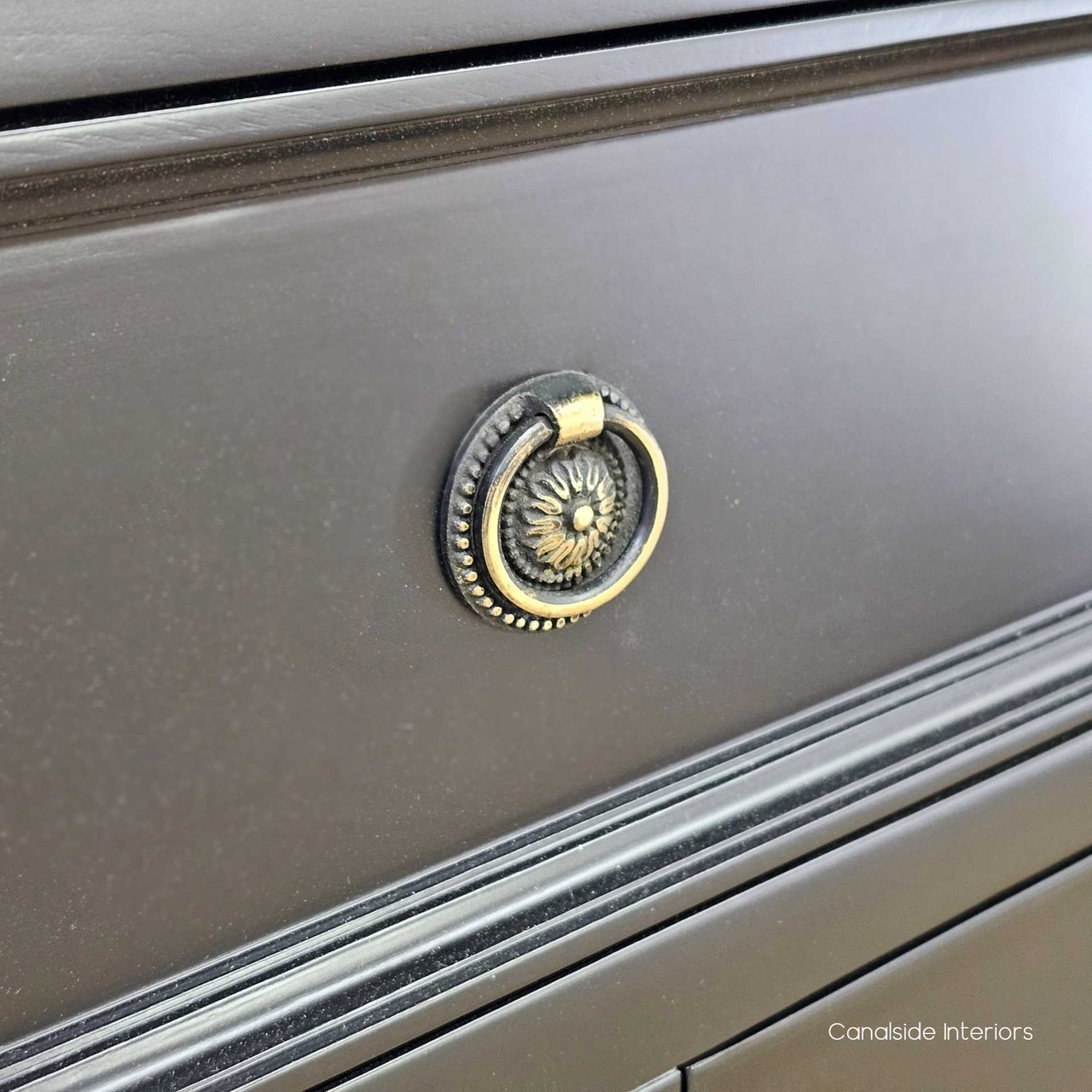 Close-up of the drawer knobs, revealing the aged brass finish and classic ring design.