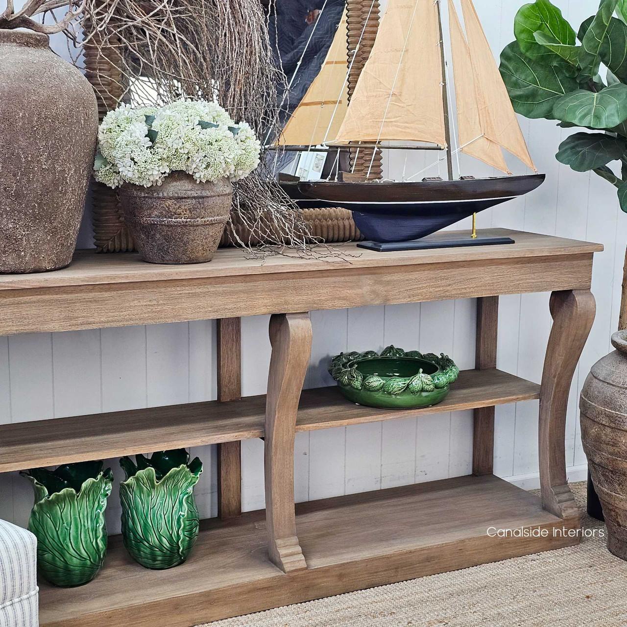 Console styled with a ship model and botanical branches, blending organic and nautical decor.