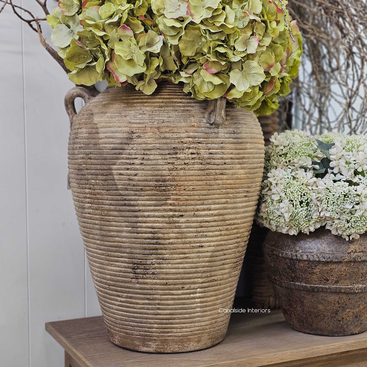 Styled on a timber console with layered florals and branches, illustrating the vessel's impact as a floor anchor.