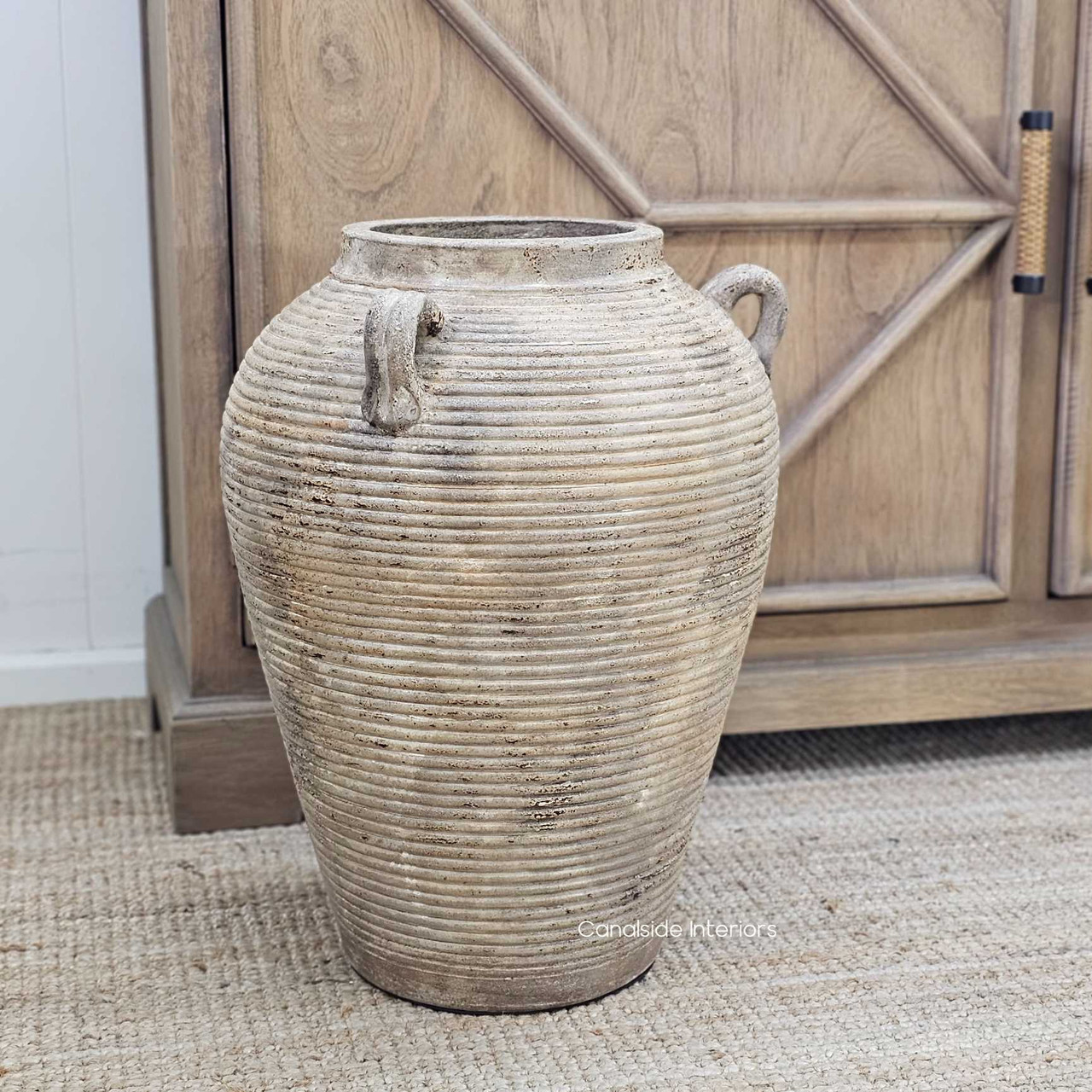 The Lirien Large Pot Terracotta Vessel displayed as a standalone floor piece, showcasing its bold sculptural form, ribbed texture, and earthy patina—ideal for anchoring open spaces with rustic elegance.