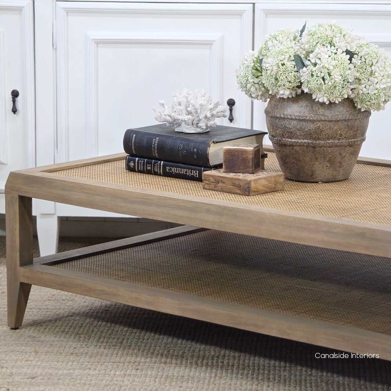 Detail of the rattan lower shelf on the Haddon Rattan Coffee Table styled with decorative books and ceramics.