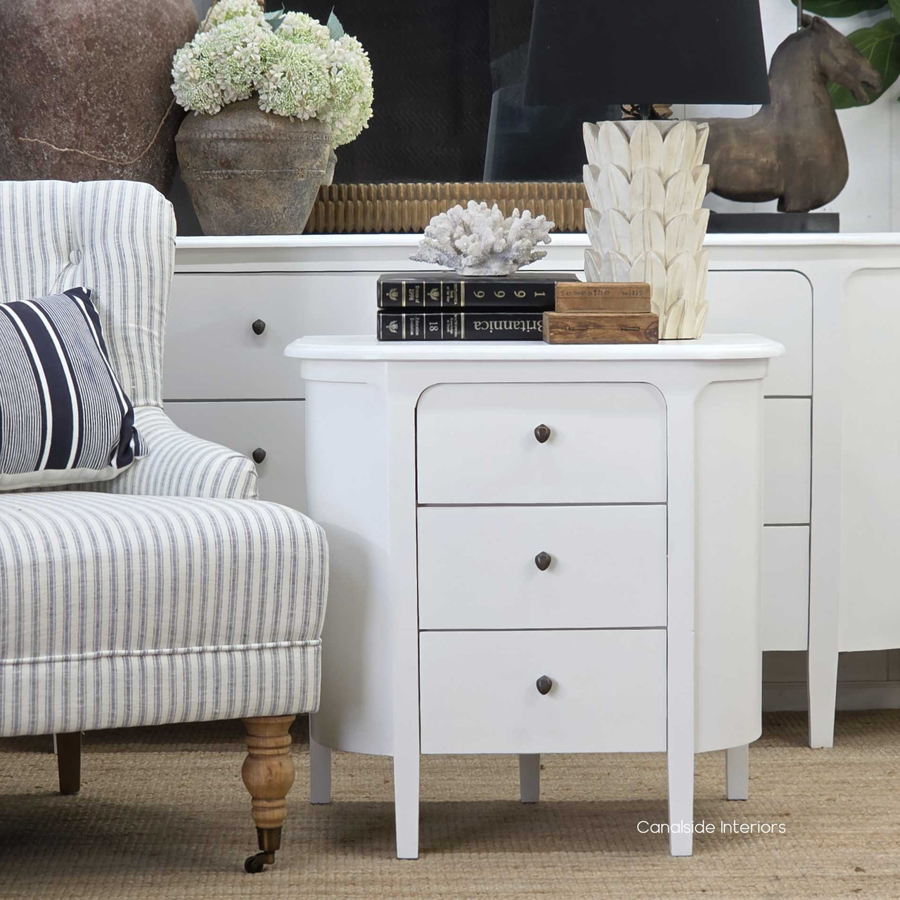 Lifestyle setting featuring the Creemore 3 Drawer Bedside in White, styled beside an armchair to highlight its soft rounded edges and clean, modern profile.