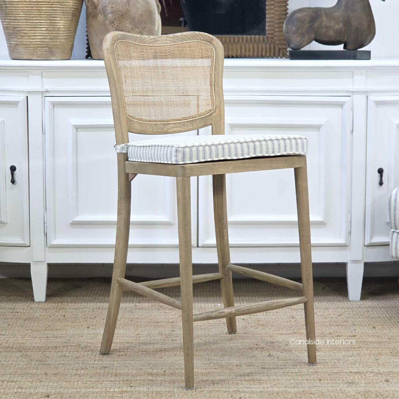 Angled view of the Noda Rattan Stool with Blue Stripe Cushion, highlighting the natural oak frame, woven rattan back and tailored ticking fabric seat.