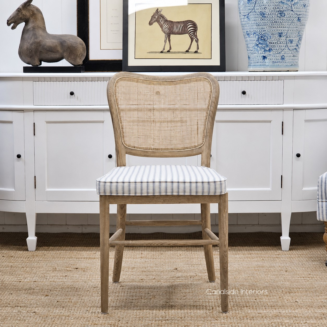 Front view of the Noda Rattan Chair with optional Blue Stripe Cushion, showcasing the classic ticking stripe, shaped seat pad and relaxed coastal styling.