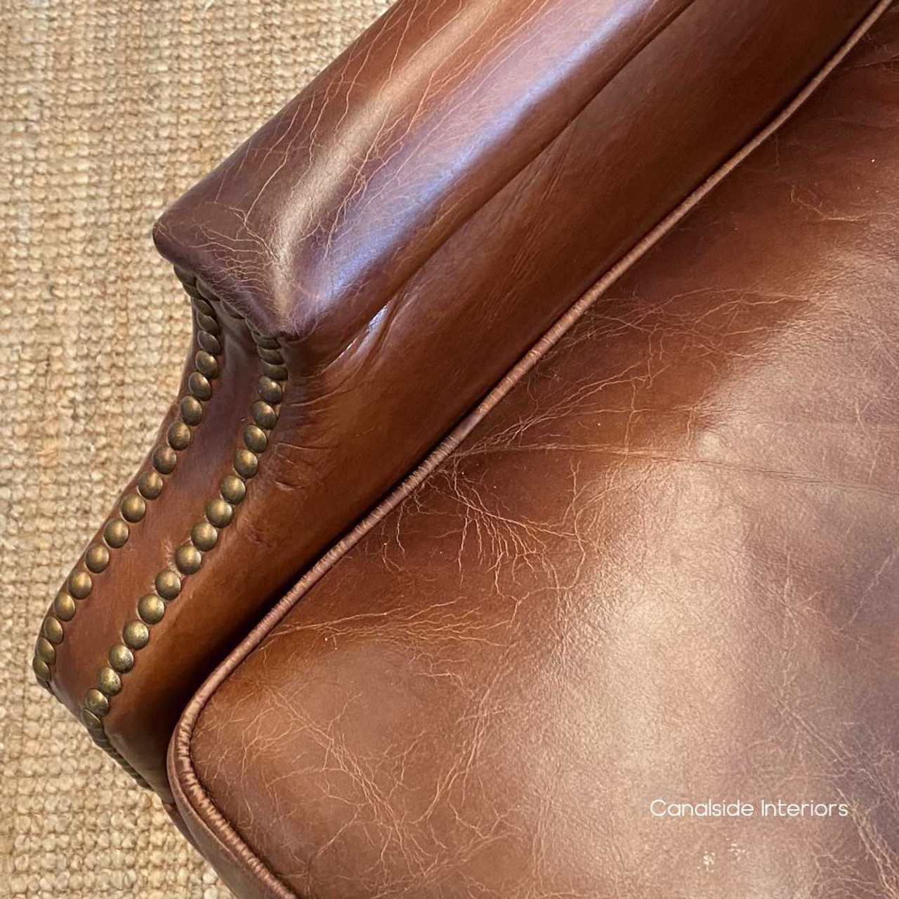 Close-up of the armchair's aged leather, highlighting the rich texture and depth of colour.