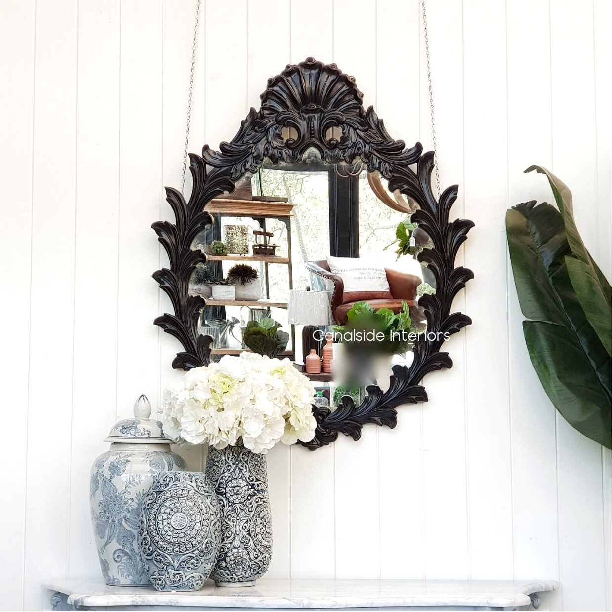 The Willow Mirror in distressed black, prominently displayed above a console table, showcasing its intricate 'fern' design against a neutral wall.