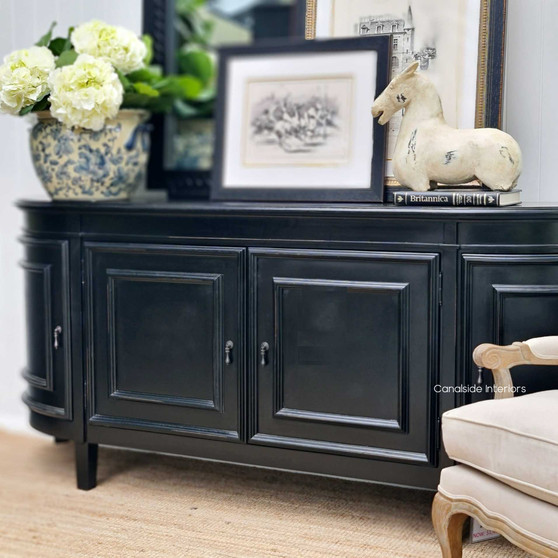 The Francia Curved Sideboard in distressed black charcoal from Canalside Interiors, with a classical silhouette perfect for enhancing the timeless elegance of a Hamptons-style bedroom