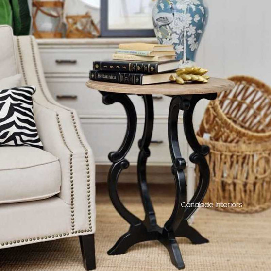 View of the Missandei Round Side Table in distressed charcoal with a weathered oak top, showcasing its unique hand-carved silhouette against a modern living room backdrop.