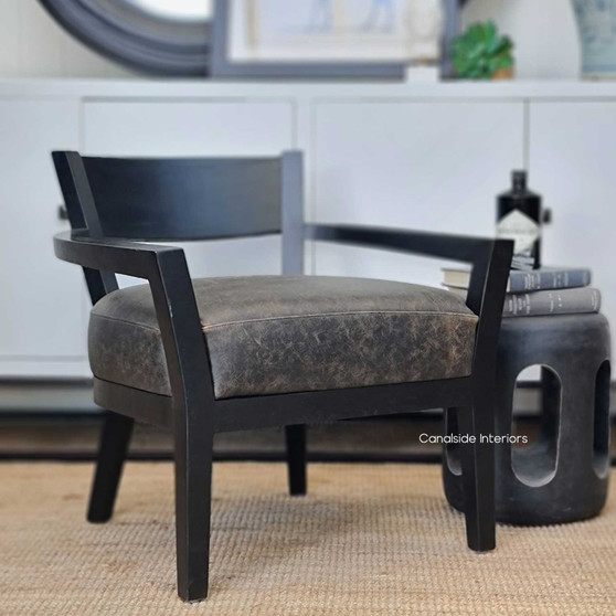The Vettel Aged Leather Armchair showcased in a sophisticated living room setting, highlighting its distressed espresso leather against a modern backdrop.