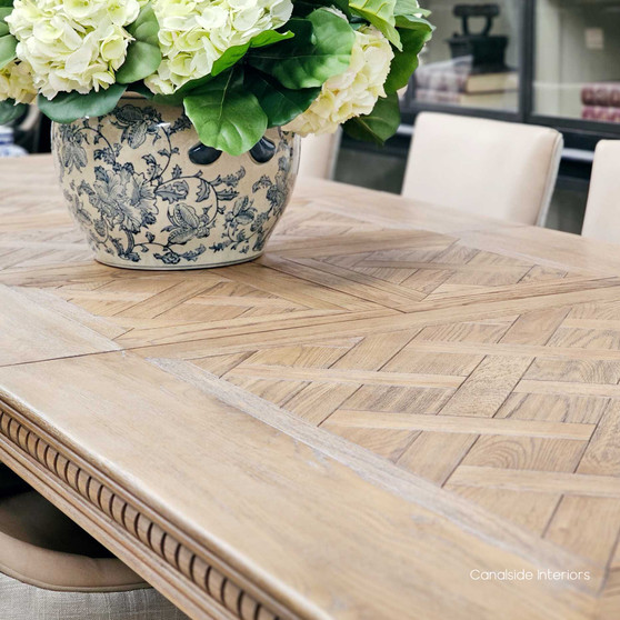 Angled perspective of the dining table, emphasizing its carved geometric apron and the richness of the oak construction