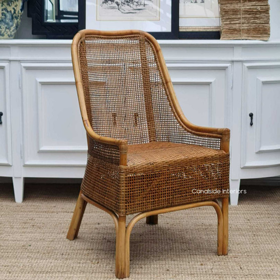 St Croix Rattan Dining Chair in full view set against a chic white cabinet backdrop, showcasing its Manuka finish and coastal Hamptons style.