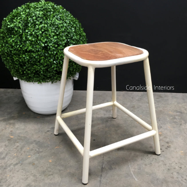 Frontal view of the Axis Industrial Low Stool with its wooden seat and metal base, showcased in a bright, modern living space.