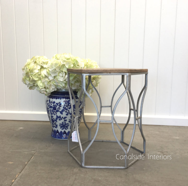 The Braxton Side Table/Stool in Distressed Industrial Silver stands against a dark wall, its geometric design adding a modern edge to Hamptons-style cafe settin