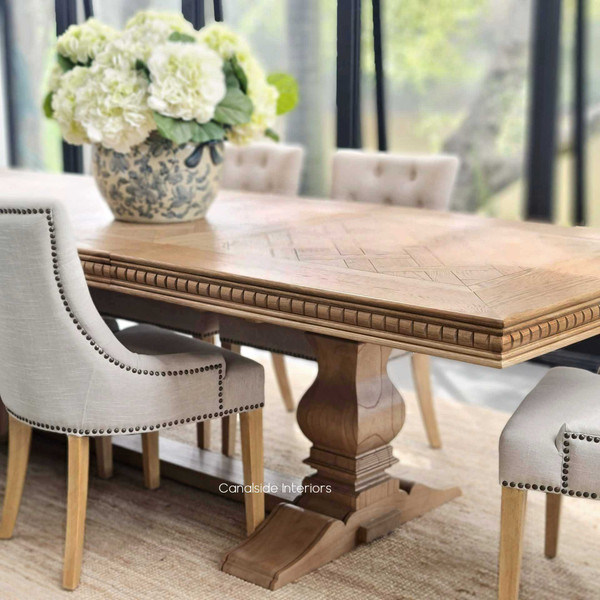 Angled perspective of the dining table, emphasizing its carved geometric apron and the richness of the oak construction