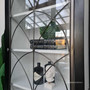 Close-up of the cabinet's glass display door, highlighting the intricate iron detailing that adds a gothic touch to the modern home.