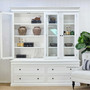 Glass doors open revealing white interior shelves filled with neutral-toned decor.