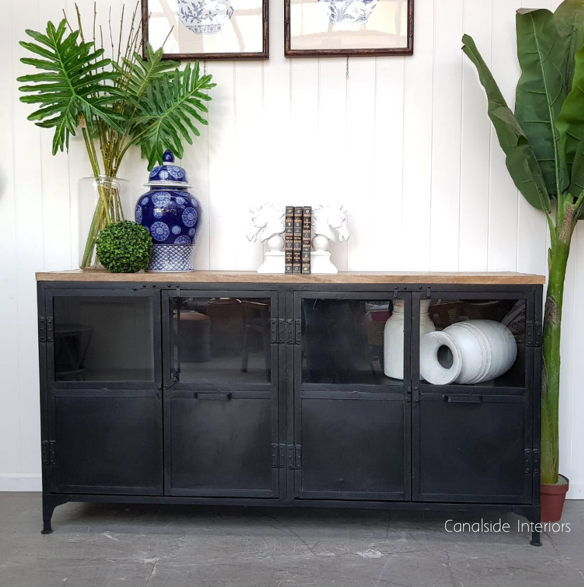 The Foundry 4 Door Industrial TV Sideboard from Canalside Interiors, featuring a distressed charcoal finish and mangowood top, combines modern industrial design with Hamptons-style luxury for your living room.