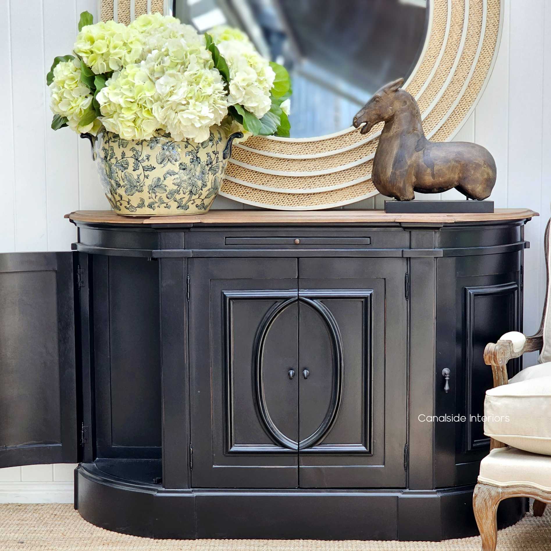 Distressed charcoal black sideboard as a focal point in a lounge room, accessorized with bright floral arrangements and Hamptons-inspired decor - Canalside Interiors