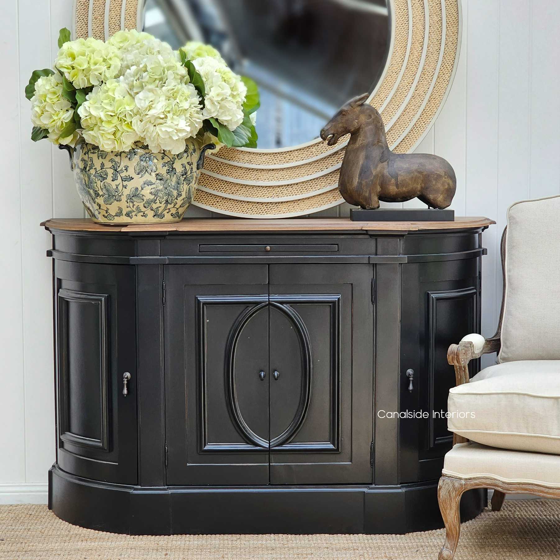 The Bastian Small Sideboard in charcoal black, standing elegantly in a serene bedroom, its weathered oak top a testament to Canalside Interiors' commitment to timeless quality.