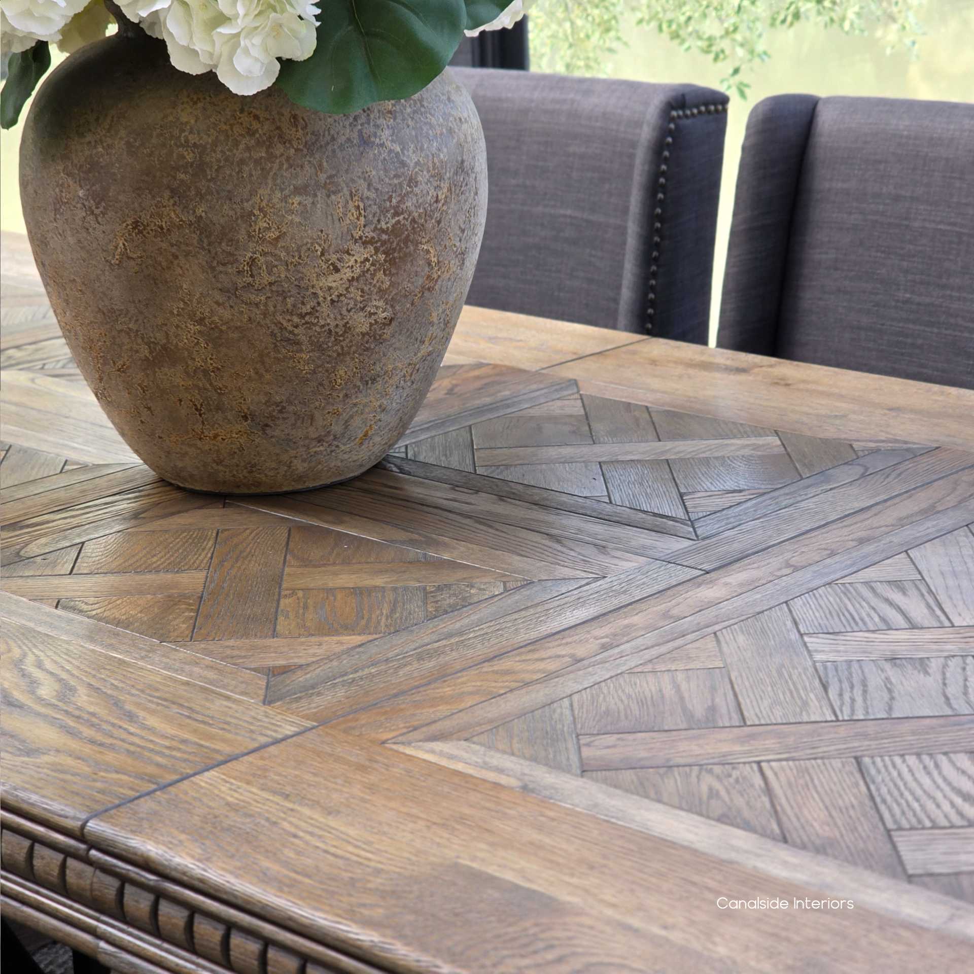 Close-up of rich Cigar oak grain on parquetry tabletop surrounded by plush upholstered dining chairs.