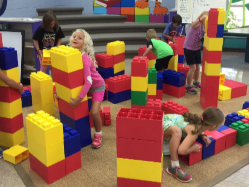 Children building tall structures with oversized, colorful plastic blocks in a play area.
