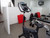 Small home gym with a stationary exercise bike, dumbbells, weight bench, and wall-mounted TV.