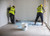 Two installers in hi-viz jackets using Ardex P51 Primer to prime a floor ready for tiling.