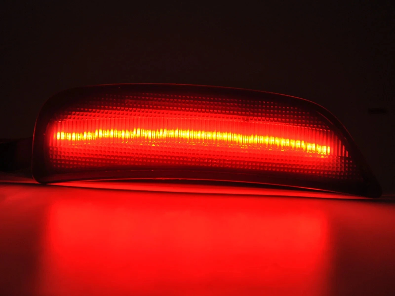 Close-up of a rear smoked side marker for an MX-5. The dark lens is centered by a horizontal, glowing red LED bar